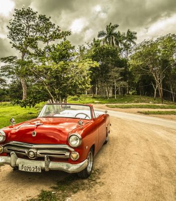 Bäume, bewölkter Himmel und ein roter klassischer Oldtimer auf  nicht asphaltierter Straße