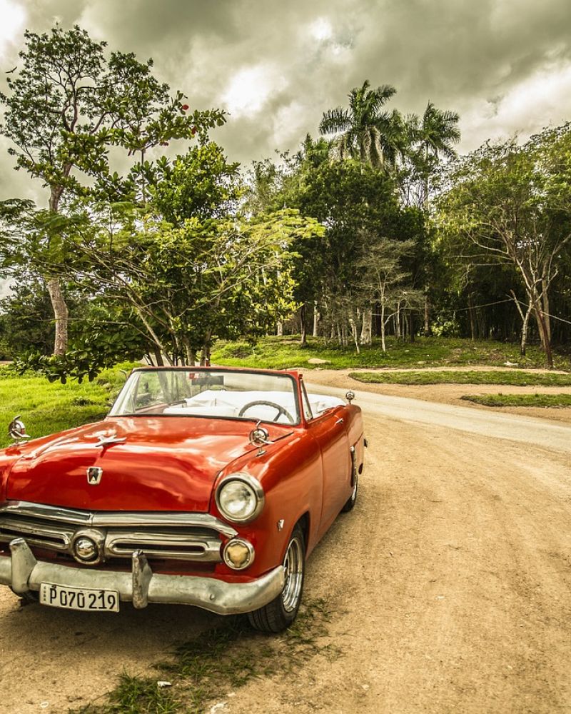 Bäume, bewölkter Himmel und ein roter klassischer Oldtimer auf  nicht asphaltierter Straße